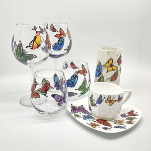 May include: Set of five glass cups and a saucer with a butterfly design. The cups are clear glass with colorful butterfly designs. The saucer is white with colorful butterfly designs.