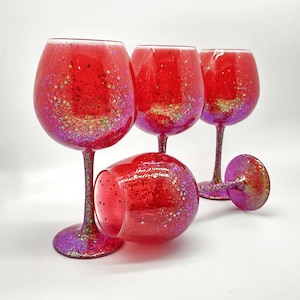 May include: Four red wine glasses with a glittery finish. The glasses are filled with a red liquid and have a clear stem.