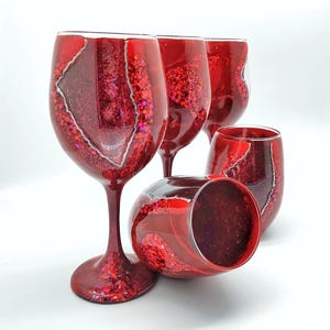 May include: Set of four red wine glasses with a glittery, agate-like design. The glasses are arranged in a group, with one glass lying on its side.