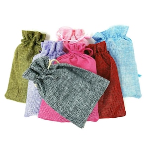 May include: A collection of small drawstring bags in various colors, including green, purple, pink, red, blue, and gray. The bags are made of a textured fabric, and each has a matching drawstring closure.