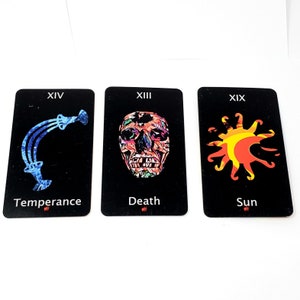 May include: Three rectangular tarot cards with black backgrounds. The first card labeled XIV Temperance features a blue abstract shape. The second card labeled XIII Death shows a colorful skull. The third card labeled XIX Sun displays a yellow and orange sun.