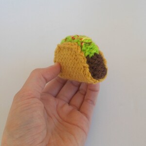 K&ouml;nnte beinhalten: Ein geh&auml;kelter Taco mit brauner F&uuml;llung, gr&uuml;nem Salat und roten und gelben Bel&auml;gen.