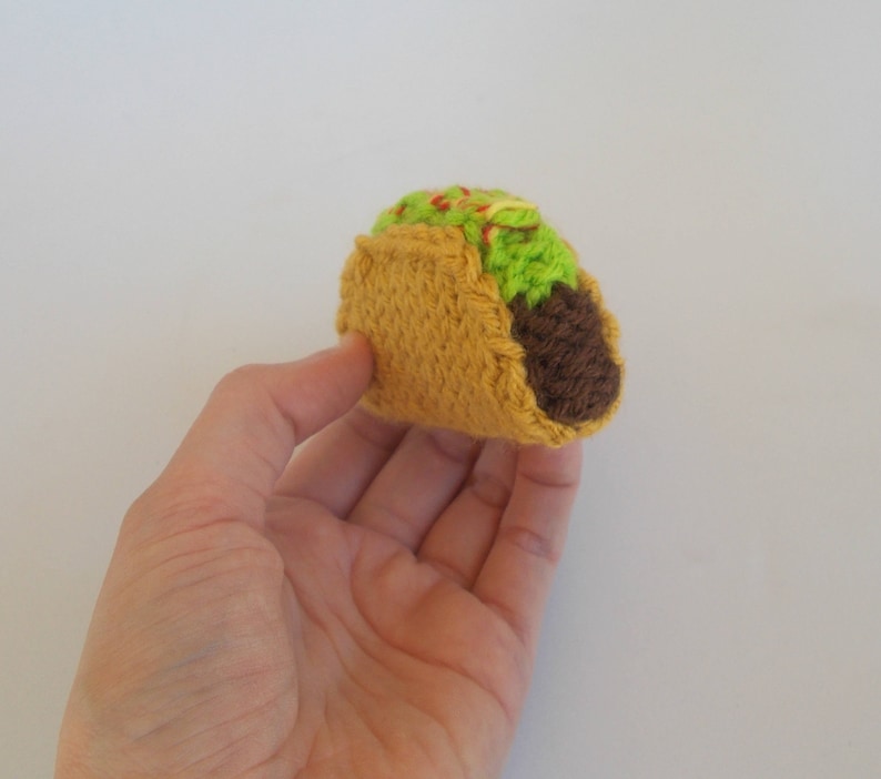 K&ouml;nnte beinhalten: Ein geh&auml;kelter Taco mit brauner F&uuml;llung, gr&uuml;nem Salat und roten und gelben Bel&auml;gen.