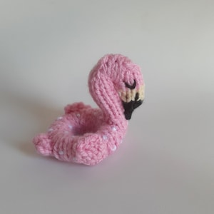 May include: A pink knitted flamingo pool float with white polka dots. The flamingo has black eyes and a black beak.
