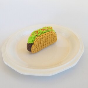 K&ouml;nnte beinhalten: Ein geh&auml;kelter Taco mit gr&uuml;nem Salat und roter Sauce auf einem wei&szlig;en Teller.