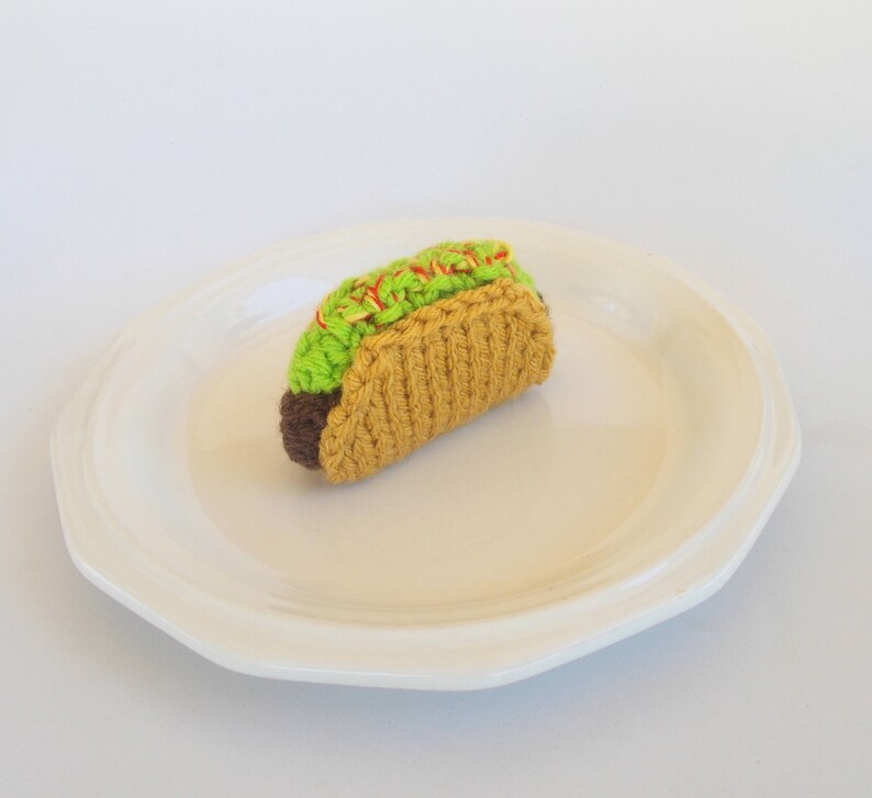 K&ouml;nnte beinhalten: Ein geh&auml;kelter Taco mit gr&uuml;nem Salat und roter Sauce auf einem wei&szlig;en Teller.