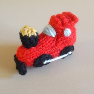 May include: A red knitted toy train with black wheels and a yellow chimney. The train has white details on the sides.