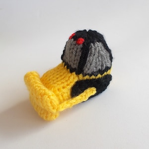 May include: A yellow knitted toy bulldozer with a black and gray cab and red eyes.