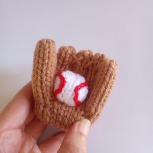May include: A brown knitted baseball glove with a white baseball with red stitching inside.