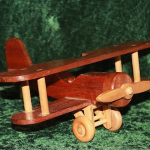 May include: A wooden toy biplane with brown wings and a red body. The plane has a propeller and wheels.