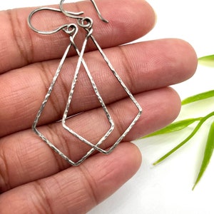May include: A pair of silver earrings with a hammered diamond shape. The earrings are simple and elegant.