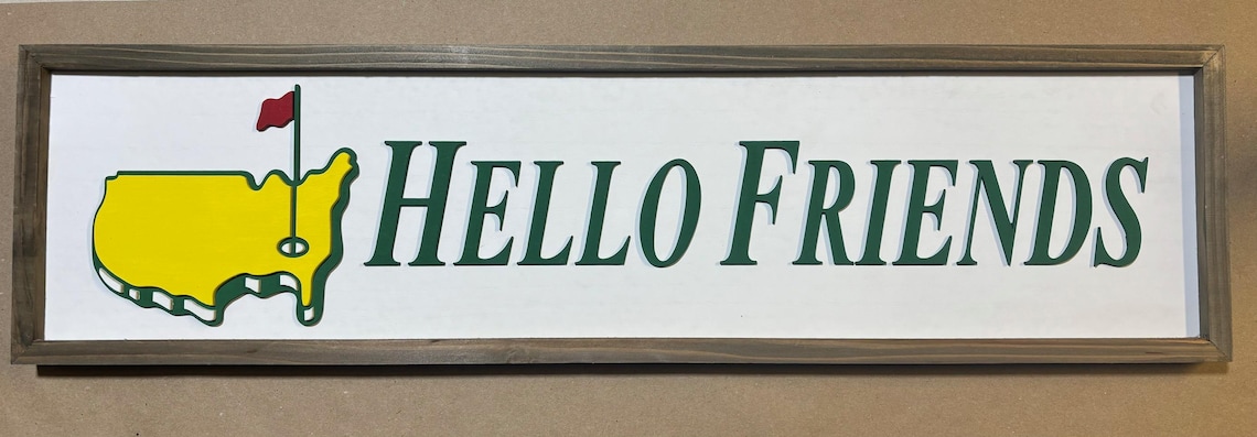 May include: A framed sign with a green and yellow outline of the United States with a red flag and golf club on top. The sign reads 'HELLO FRIENDS' in green letters.