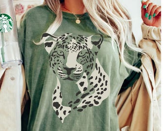 May include: A green oversized t-shirt with a white and black leopard print graphic. The shirt has a crew neck and is made of a soft, comfortable fabric. The text "Moss" is printed on the bottom of the shirt.