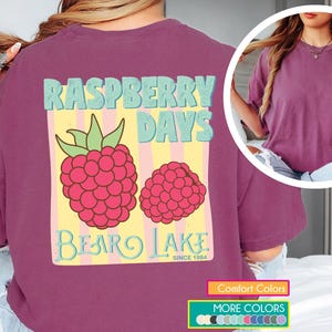 May include: A maroon t-shirt with a graphic featuring the text "Raspberry Days" above two raspberries and the text "Bear Lake Since 1984". The shirt has a crew neck and short sleeves. Additional color options are shown.