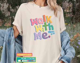 Puede incluir: Camiseta color crema con el texto "Walk With Me" en letras coloridas. El texto incluye "Moses 6:34". Esta camiseta forma parte de una colección de ropa.
