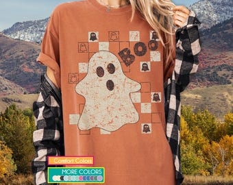 May include: A burnt orange t-shirt with a distressed ghost design, the word "BOO", and small ghost graphics. The shirt has a vintage look and is part of a Halloween-themed collection.