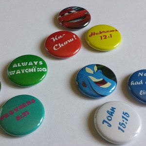 May include: Assortment of colorful round buttons with various images and text.  The buttons feature a cartoon car, a genie, a pair of sunglasses, and text including "Ka-Chow!" "Always Watching", "Proverbs 8:21", "Hebrews 12:1", "John 15:15", and "Never had a friend like me!"