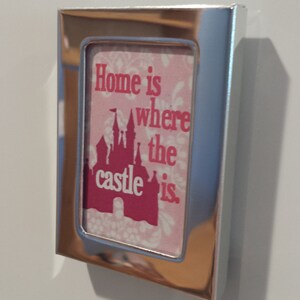 May include: A silver picture frame with a pink and white background. The frame has a quote that reads "Home is where the castle is." The castle is a pink silhouette of a Disney castle.