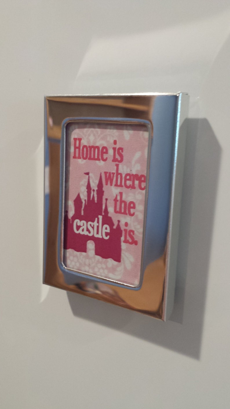 May include: A silver picture frame with a pink and white background. The frame has a quote that reads "Home is where the castle is." The castle is a pink silhouette of a Disney castle.