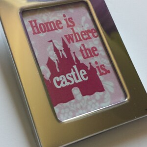 May include: A silver picture frame with a pink and red print inside. The print features a silhouette of a castle and the text "Home is where the castle is."