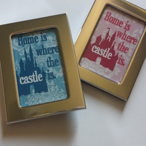 May include: Two silver framed pictures with a blue and pink background. The pictures feature a silhouette of a castle and the text "Home is where the castle is."