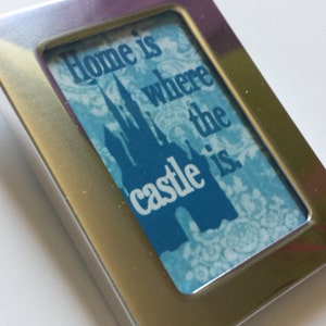 May include: A silver picture frame with a blue and white image of a castle and the text "Home is where the castle is."