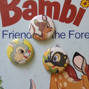 May include: Three round pinback buttons featuring characters from Disney's Bambi. The buttons are yellow, white, and black with images of Bambi, Thumper the rabbit, and Flower the skunk.