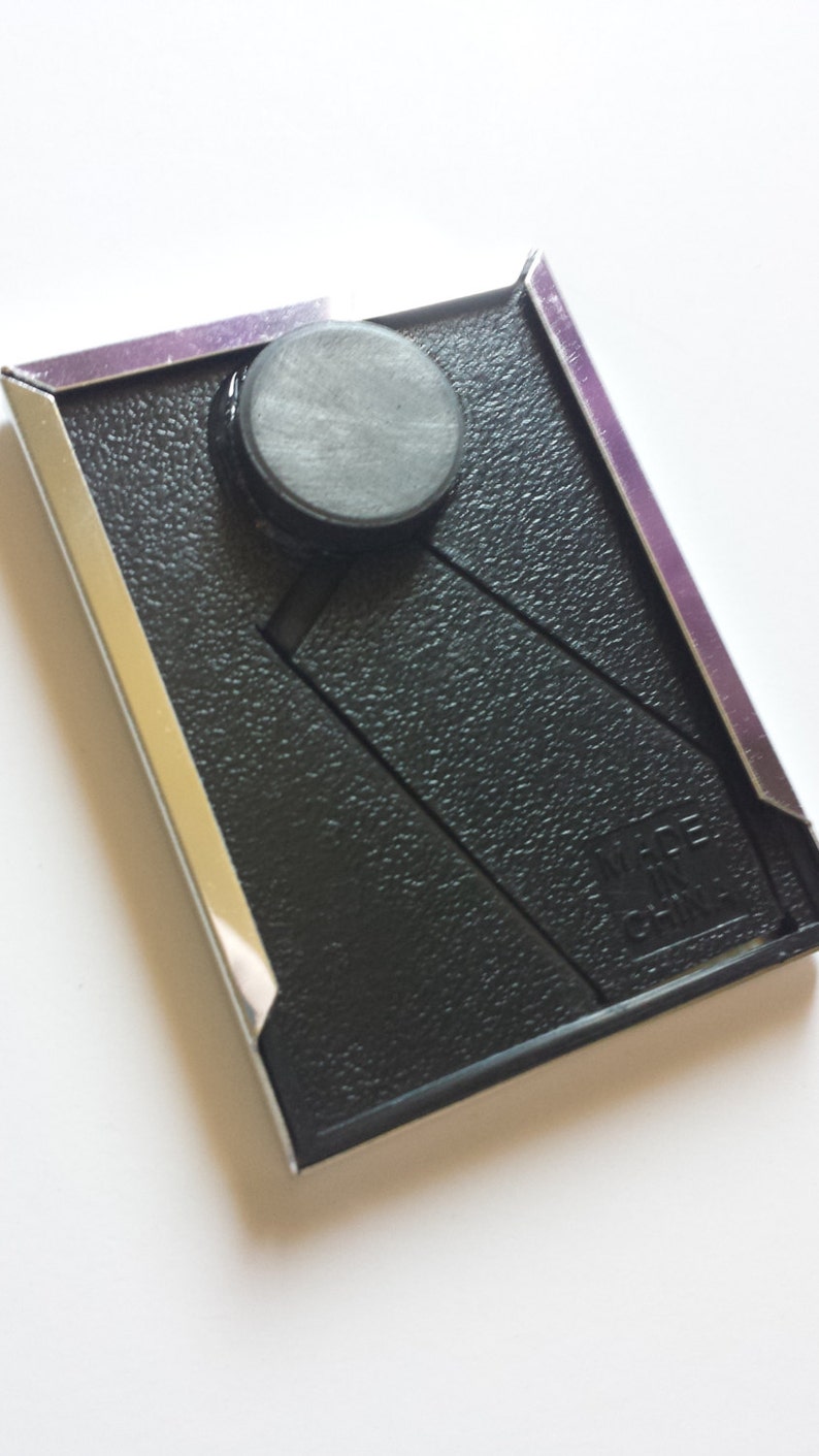 May include: A black picture frame with a silver border and a black magnet on the front. The frame has a textured surface and the text "WIRE CHAIN" is visible in the bottom right corner.