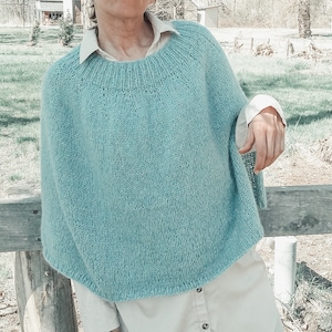 May include: A light blue knitted poncho with a round neckline. The poncho is made of a soft, fuzzy yarn and has a relaxed fit.