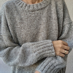 May include: A gray knitted sweater with a round neckline and long sleeves.