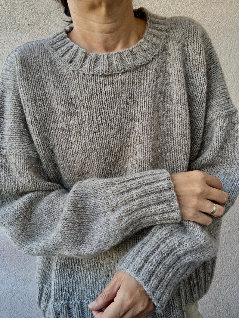 May include: A gray knitted sweater with a round neckline and long sleeves.
