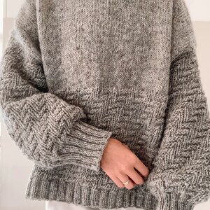 May include: A gray knitted sweater with a textured pattern. The sweater has a round neckline and long sleeves.