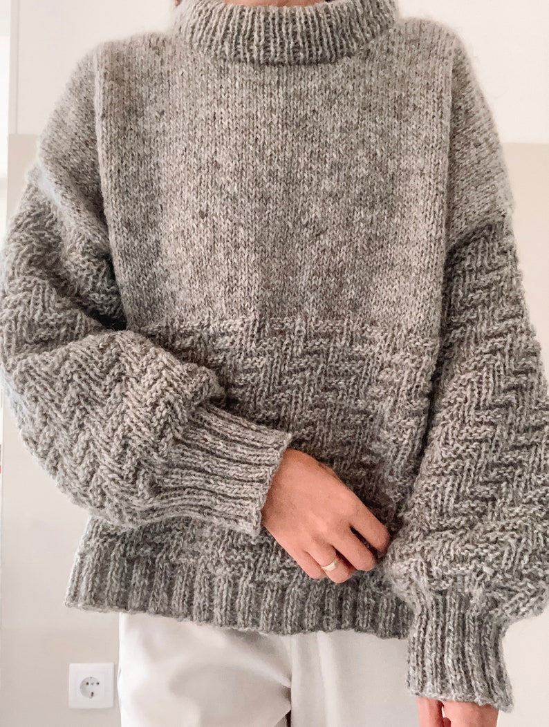 May include: A gray knitted sweater with a textured pattern. The sweater has a round neckline and long sleeves.