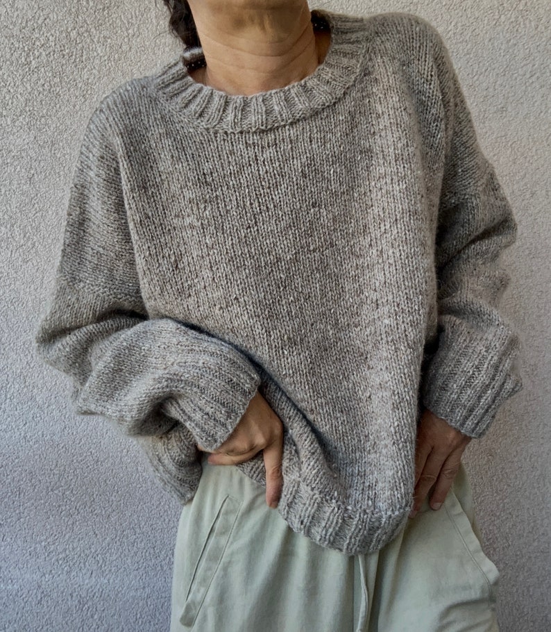 May include: A gray knitted sweater with a crew neck and long sleeves. The sweater is made of a soft, textured yarn.