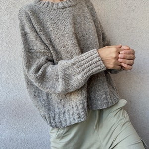May include: A gray oversized knit sweater with a crew neck and long sleeves.