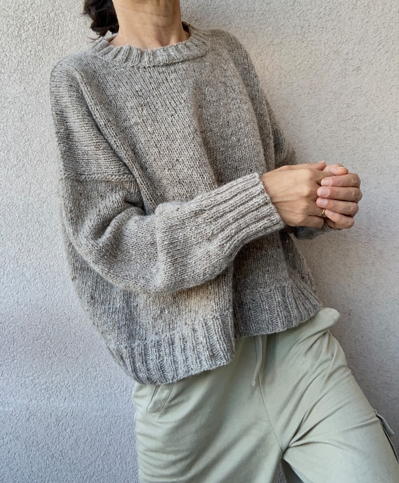 May include: A gray oversized knit sweater with a crew neck and long sleeves.