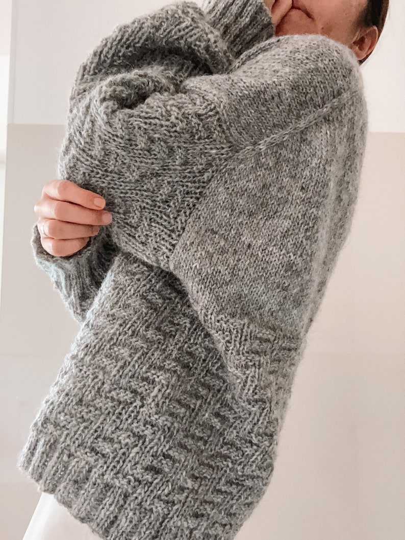 May include: A gray knitted sweater with a loose fit and a textured pattern.