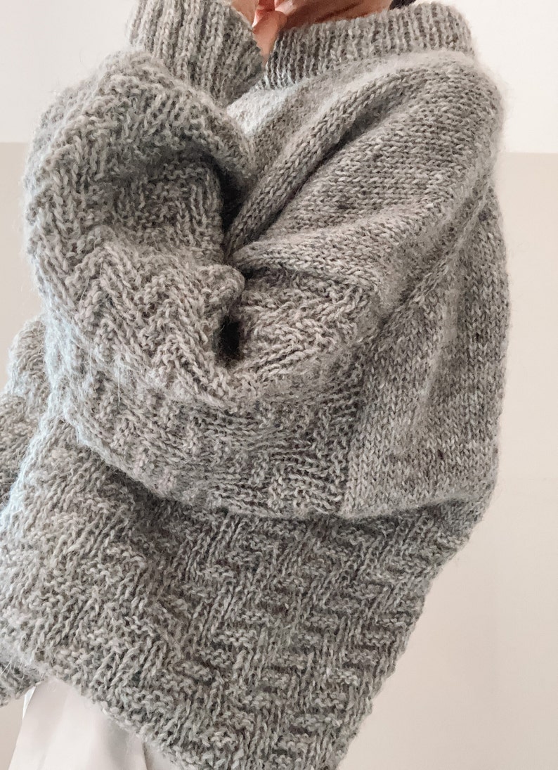May include: A gray knitted sweater with a loose fit and a textured pattern.