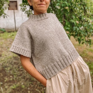 May include: A loose-fitting, short-sleeved, grey knitted sweater with a high neckline.