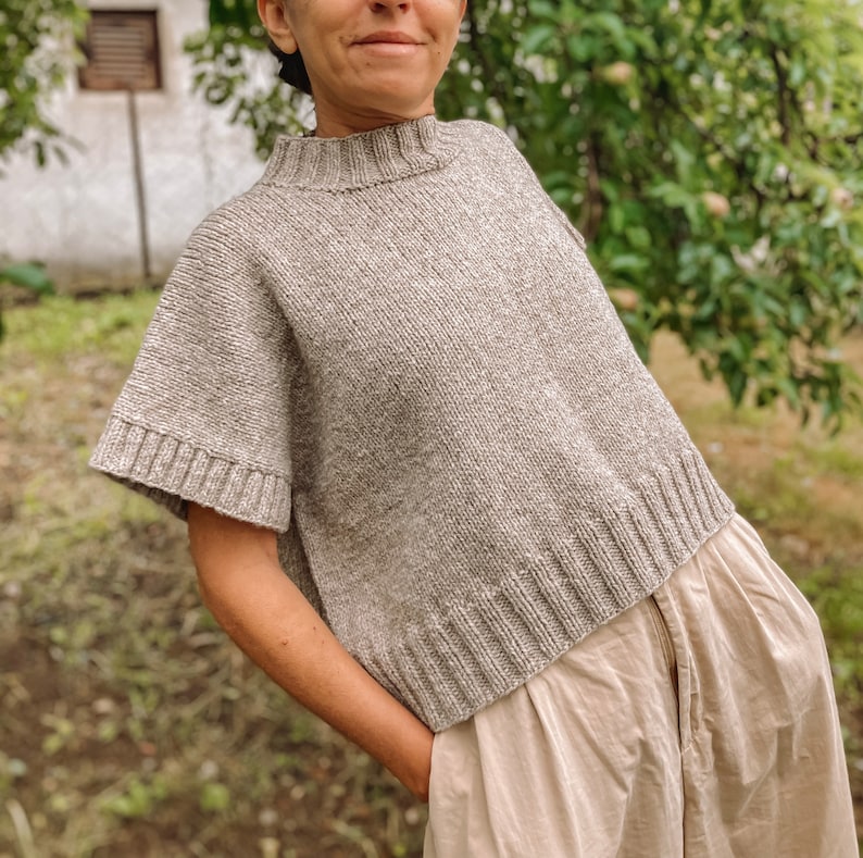 May include: A loose-fitting, short-sleeved, grey knitted sweater with a high neckline.