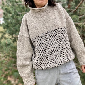 Puede incluir: Un su&eacute;ter beige de cuello alto con un patr&oacute;n de chevron blanco y negro en la mitad inferior.