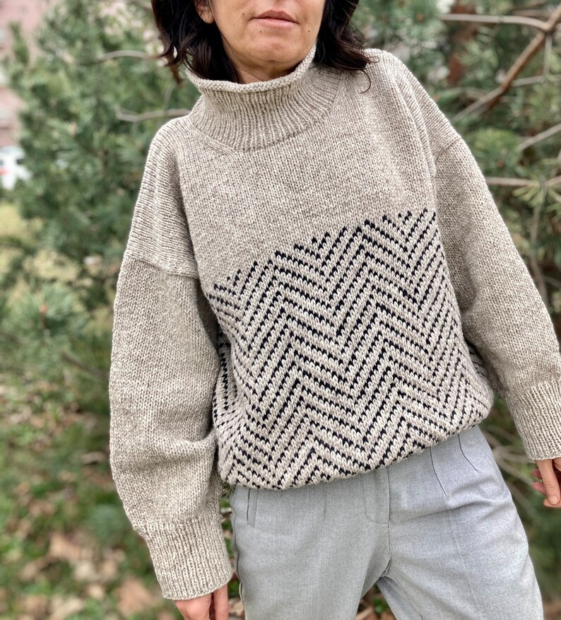 Puede incluir: Un su&eacute;ter beige de cuello alto con un patr&oacute;n de chevron blanco y negro en la mitad inferior.