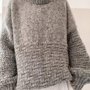 May include: A gray knitted sweater with a textured pattern on the bottom. The sweater has a high neck and long sleeves.