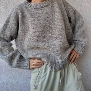 May include: A gray speckled knit sweater with a round neckline. The sweater is loose fitting and has long sleeves.