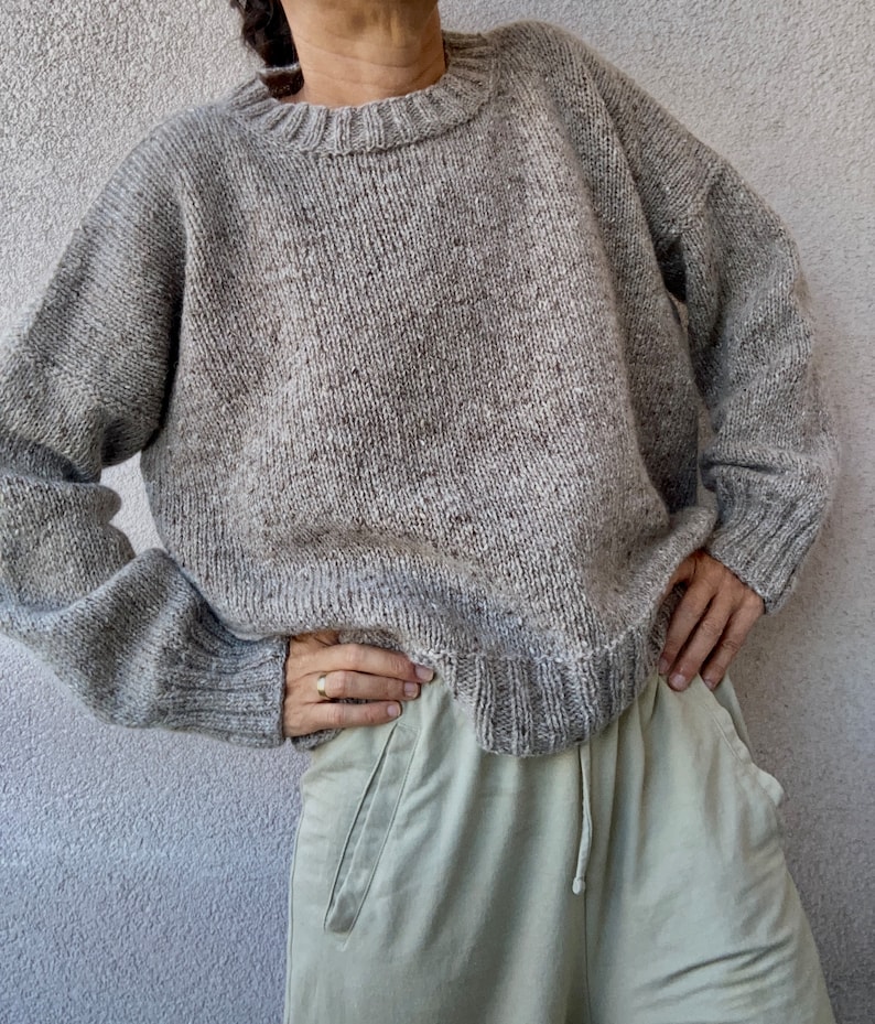 May include: A gray speckled knit sweater with a round neckline. The sweater is loose fitting and has long sleeves.