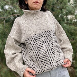 Puede incluir: Un su&eacute;ter beige de cuello alto con un patr&oacute;n de chevron negro y blanco en la mitad inferior.