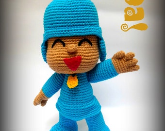 Puede incluir: Un juguete de crochet azul con una cara marrón, una boca roja y una insignia amarilla. El juguete lleva un sombrero azul y tiene una expresión amigable.