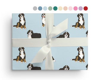 May include: Blue wrapping paper with a repeating pattern of Bernese Mountain Dogs. The dogs are brown, black, and white and are facing forward. The paper is tied with a white ribbon.