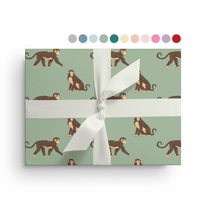May include: Green wrapping paper with a repeating pattern of brown monkeys. The monkeys are in various poses, some walking, some sitting, and some looking up. The paper is tied with a white ribbon.
