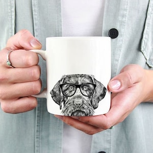 May include: White ceramic mug with a black and white illustration of a dog wearing glasses. The dog is looking directly at the viewer.